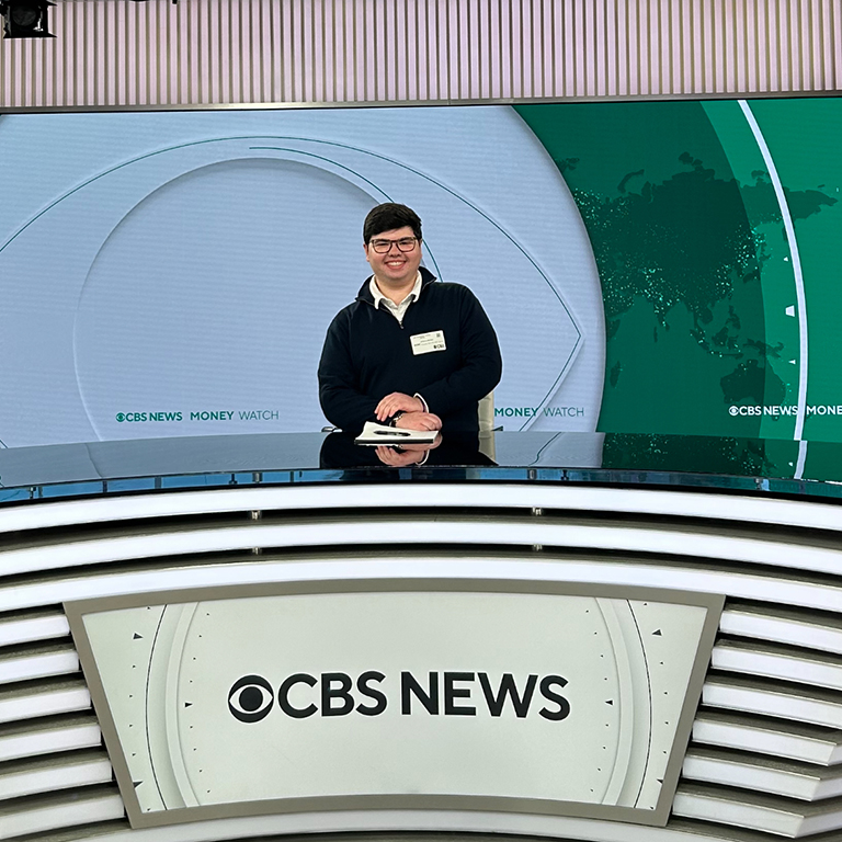 A student stands behind a CBS News news desk.