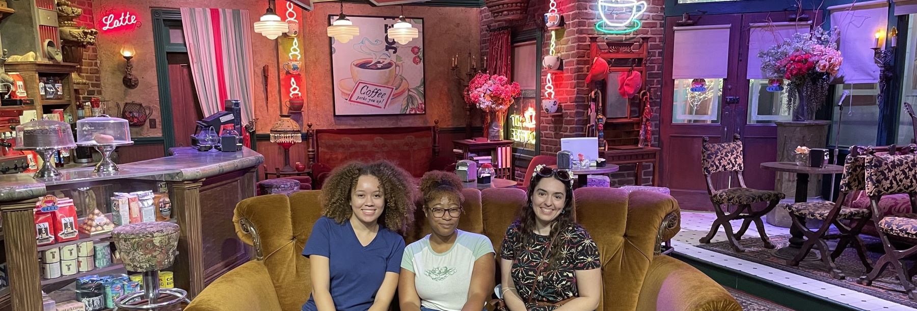 Three people sit on the coffee shop set of the TV show Friends.